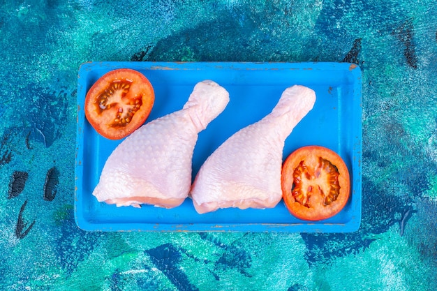 Free Photo sliced tomatoes and uncooked chicken drumstick on a wooden plate