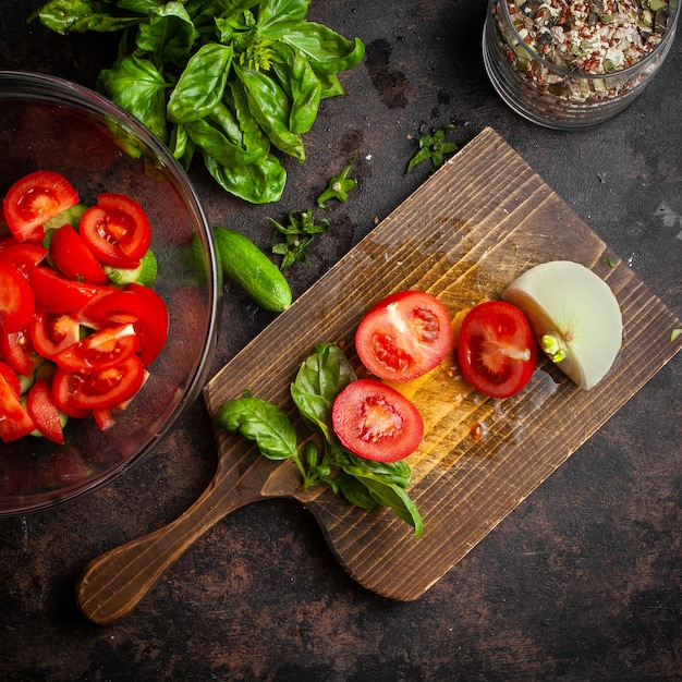 Sliced vegetables set in a glass bowl from tomatoes, cucumbers with jar of grains, onion and spinach top view on dark and chopping board