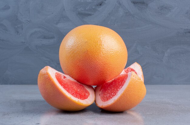 Sliced and whole grapefruits displayed on marble background. 