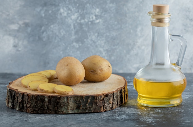 Sliced and whole potatoes on wooden board with oil.