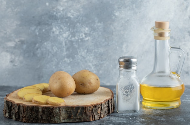 Sliced and whole potatoes on wooden board with salt and oil.