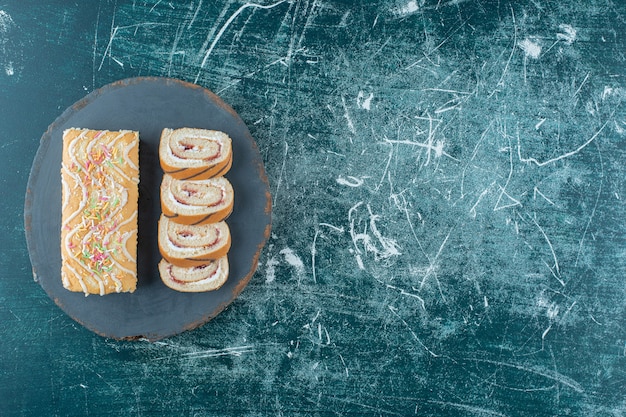 Free photo sliced and whole roll cakes on a board, on the blue background. high quality photo