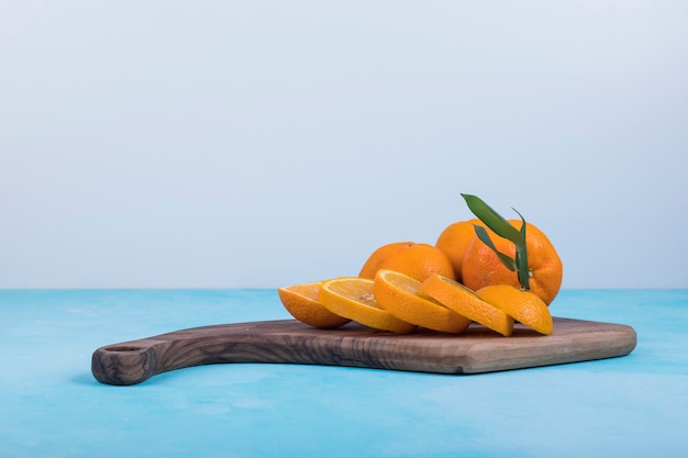 Free photo sliced yellow oranges on a wooden platter on blue, side view.