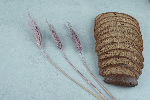 Free photo slices of black bread on stone surface with wheat