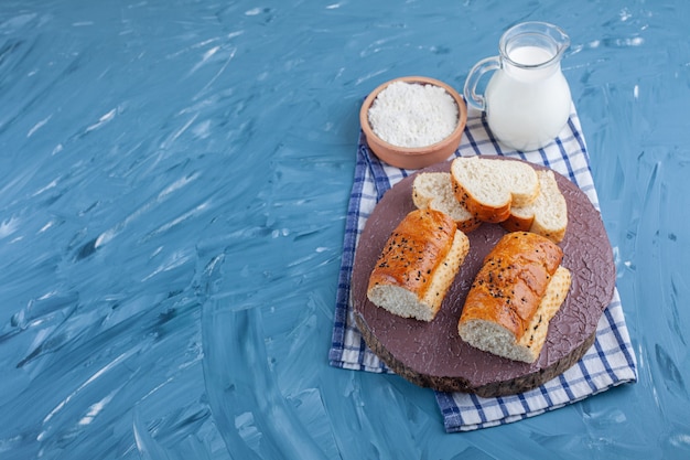 Slices of bread on a board next to boiled egg and a bowl of flour on a towel, on the blue table.