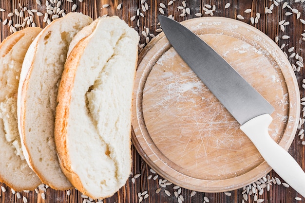 Slices of bread and sunflower seeds on wooden chopping board with knife