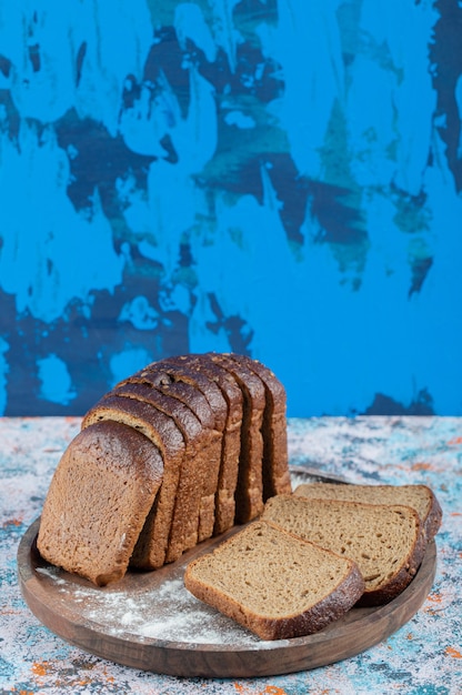 Slices of brown bread with flour on wooden round board.