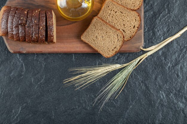 Slices of brown bread with wheat on wooden board.