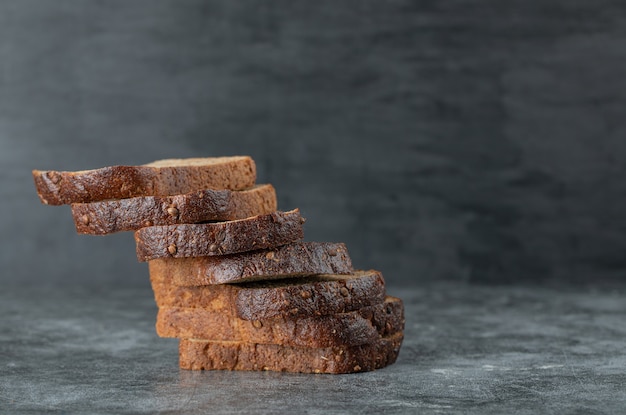 Slices of brown fresh bread on a gray background.