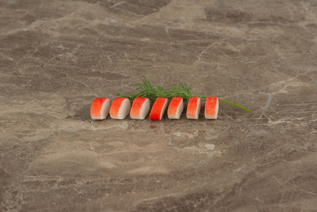 Slices of crab sticks with greens on marble table .