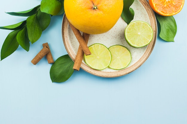 Slices of fresh exotic fruits near cinnamon on plate with foliage