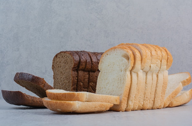 Slices of fresh white and brown breads on marble background.