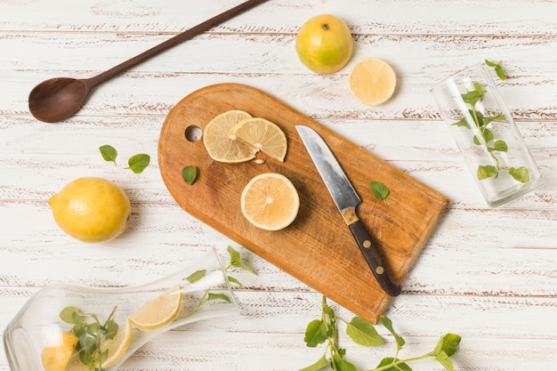 Free photo slices of fruits near knife between herbs and glasses