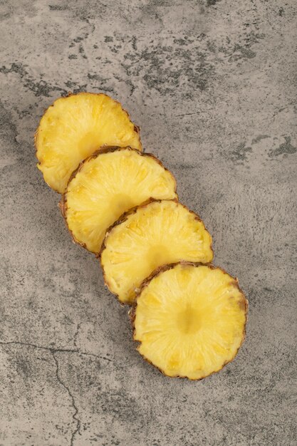 Slices of juicy delicious pineapple placed on stone surface.