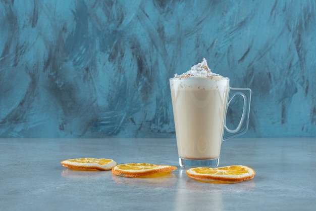 Slices lemon next to a cup of cappuccino , on the blue table. 