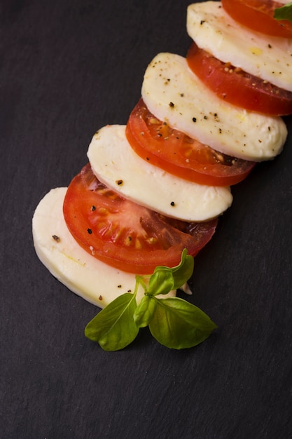 Free photo slices of mozzarella cheese and tomatoes with pepper seasoning and herbs on black background