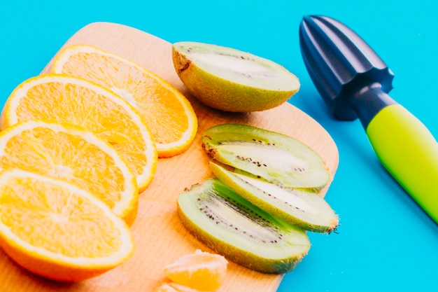 Free photo slices of oranges and kiwi slices and hand juicer on blue background