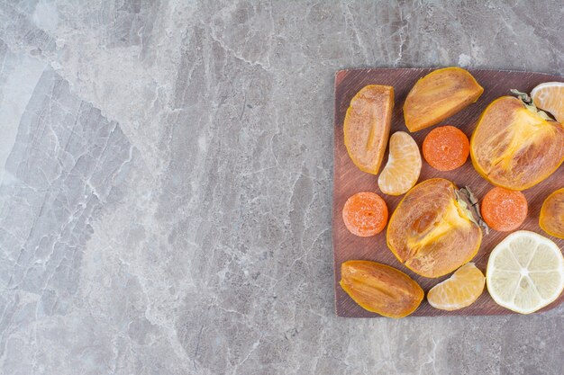 Slices of persimmon, lemon, tangerine and candies on board. 