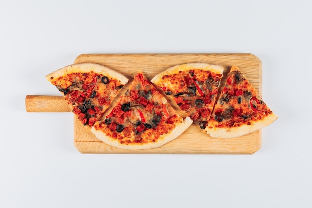 Slices of a pizza in a pizza board on a bright white stucco background. flat lay.