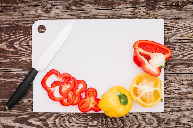 Free photo slices of red bell peppers with sharp knife on white board over the wooden tabletop