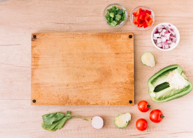 Slices of red; green bell pepper; onion; beet root; cherry tomatoes near the blank chopping board over the wooden desk