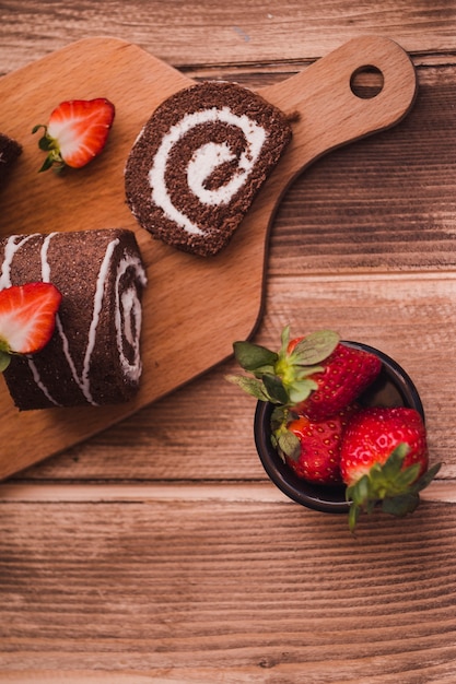 Slices of tasty roll and strawberries on wooden table