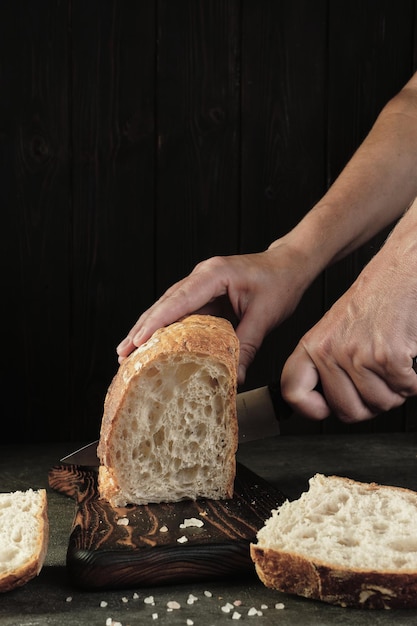 Free photo slicing bread on a wooden board isolated on a dark background woman cuts fresh artisan bread on the kitchen table vertical frame healthy food and traditional bakery concept