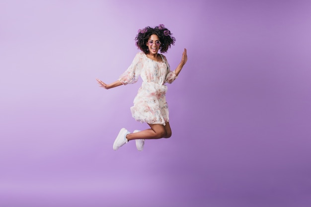 Slim african woman in white sneakers jumping and laughing. Indoor photo of good-humoured black girl dancing.