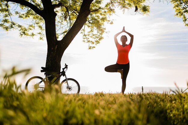 Slim beautiful woman silhouette doing sports in morning in park doing yoga