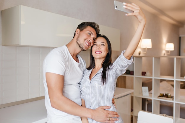 Slim dark-haired woman making selfie with husband before breakfast