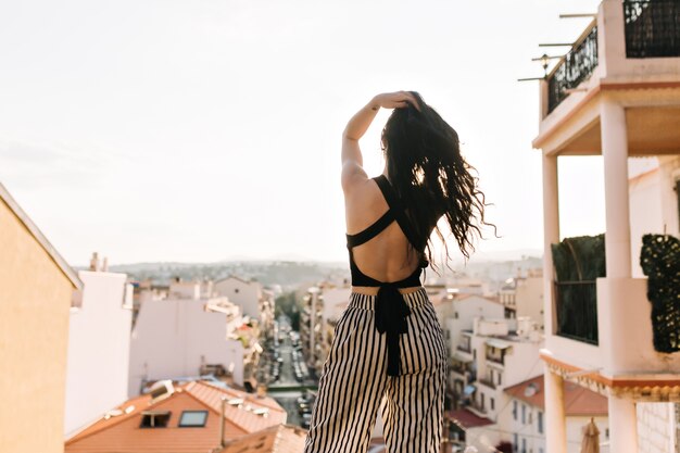 Slim elegant girl with long dark hair enjoying city views from observation deck in morning