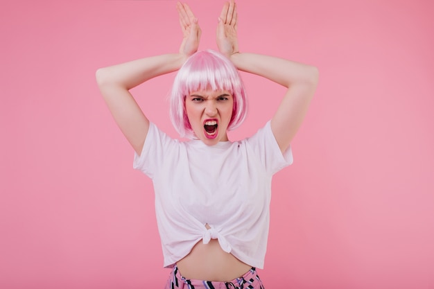 Free Photo slim emotional lady in pink hair fooling around . indoor shot of pretty female model isolated on pastel wall