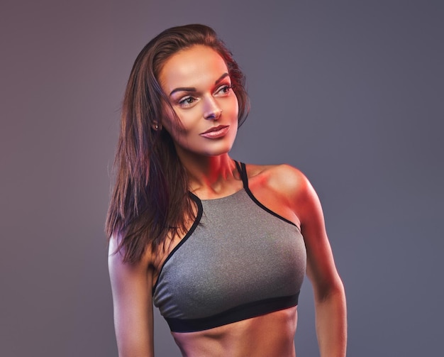 Slim fitness brunette woman in a gray sportswear posing in a studio. Isolated on a gray background.