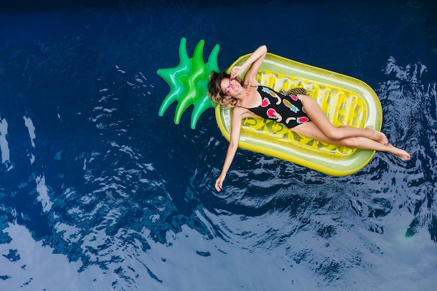 Free Photo slim girl with tanned skin laughing while lying on mattress at sea resort. outdoor photo of good-looking female model in sparkle sunglasses.