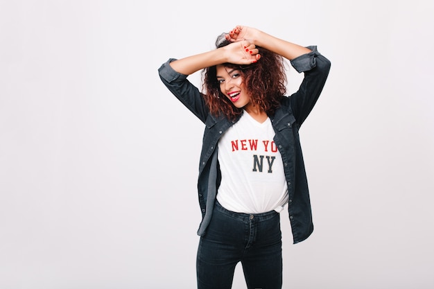 Free photo slim inspired girl in denim pants pretty dancing and laughing. happy black young woman with red manicure posing with hands up having fun.