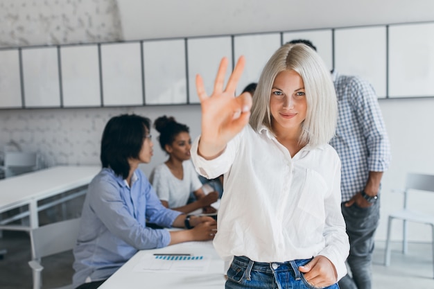 Free Photo slim woman with blonde short hair showing okay sign after succesful negotiation. portrait of asian office worker posing with african colleague during conference with fair-haired woman.