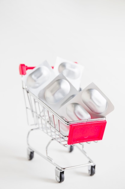 Free photo sliver blister pills in the miniature shopping cart on white background