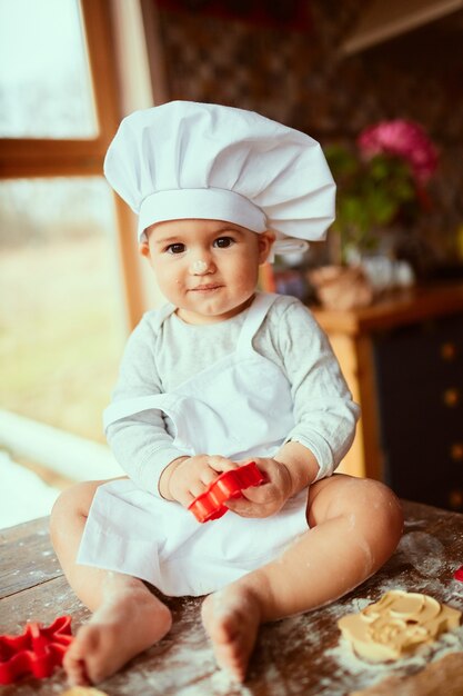 The small baby sits on the table near dough