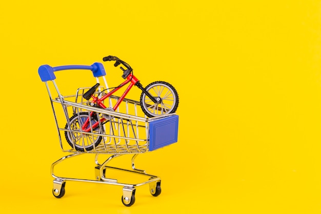 Free photo small bicycle toy in the shopping cart against yellow background