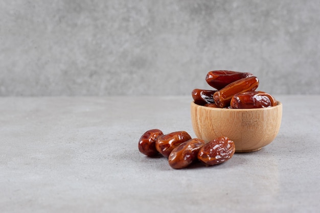 A small bowl of dates next to a handful on marble background. High quality photo