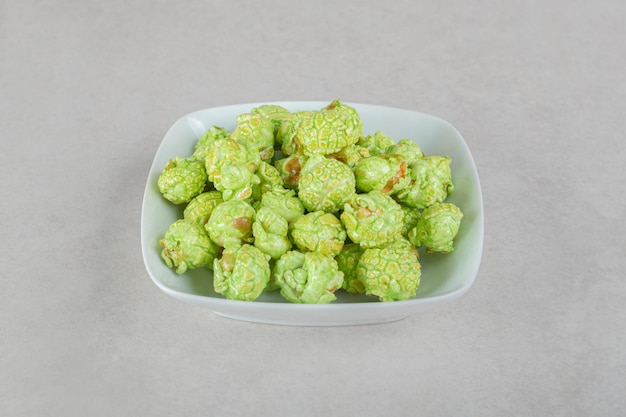 Small bowl of green candied popcorn on marble table.