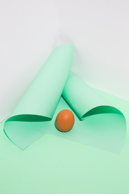 Free Photo small brown chicken egg with rolled papers on green table