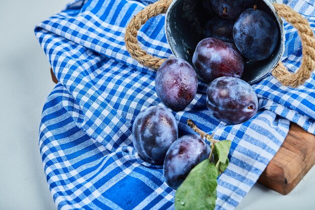 Small bucket of garden plums on blue tablecloth.