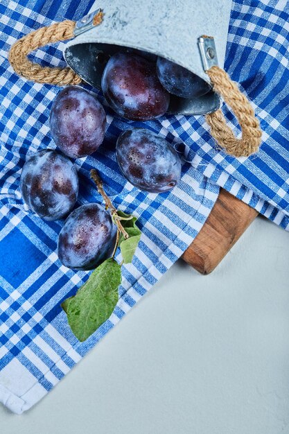 Small bucket of garden plums on blue tablecloth.