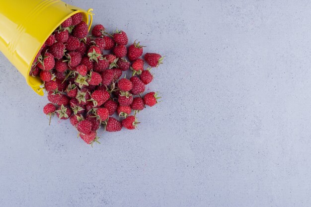 Small bucket of raspberries spilled over on marble background. High quality photo