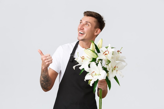 Free photo small business retail and employees concept handsome florist salesman in flower shop pointing upper ...