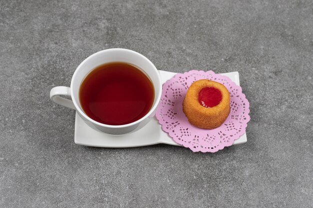 Small cake with jelly and cup of tea on marble surface