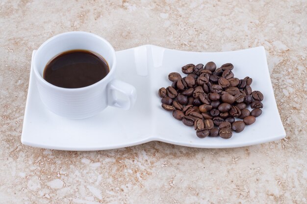 A small cup of coffee next to a pile of coffee beans 