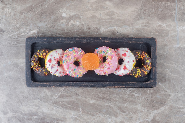 Small donuts and a marmelade bundled on a black tray on marble surface