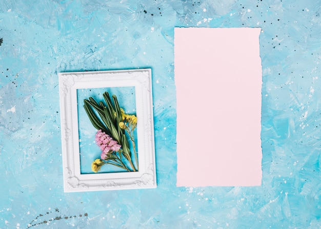 Small flowers branches in frame with blank paper on table 